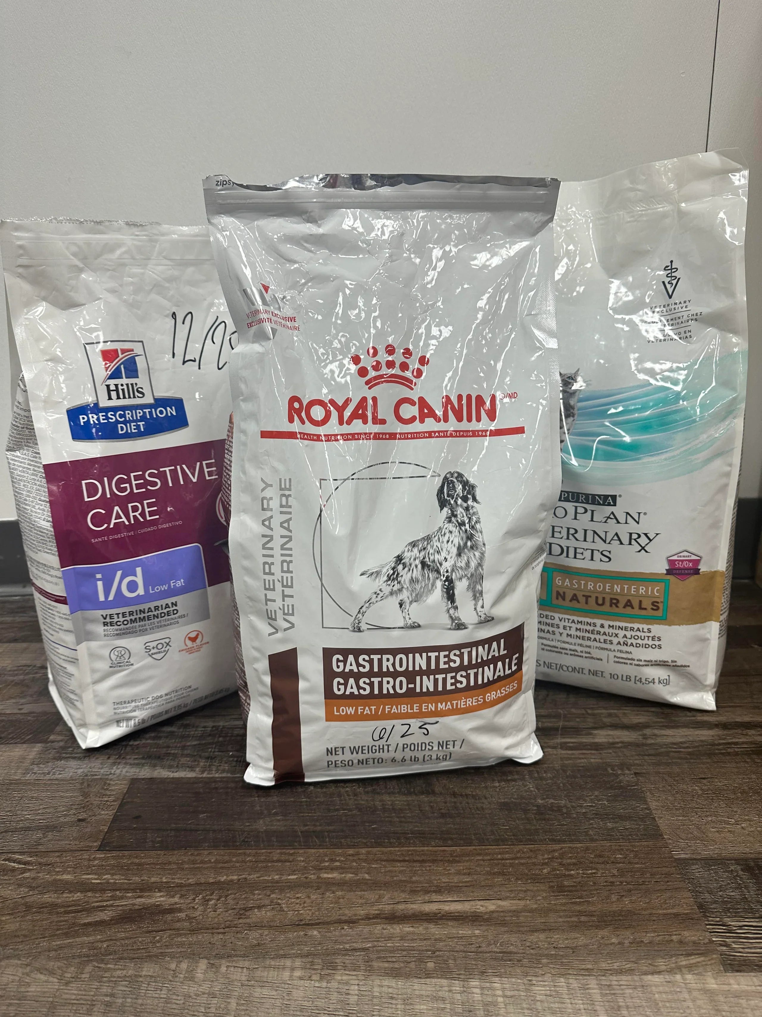 Three bags of Royal Canin veterinary diet products on a wooden surface.